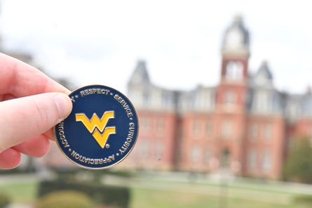 The WVU Values Coin being held in front of Woodburn Hall