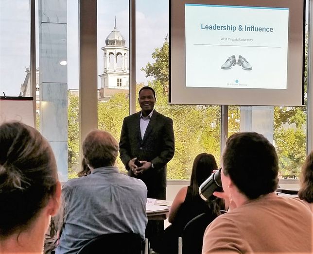 JD Williams Standing in front of projector screen reading Leadership and influence with Woodburn Hall tower in background